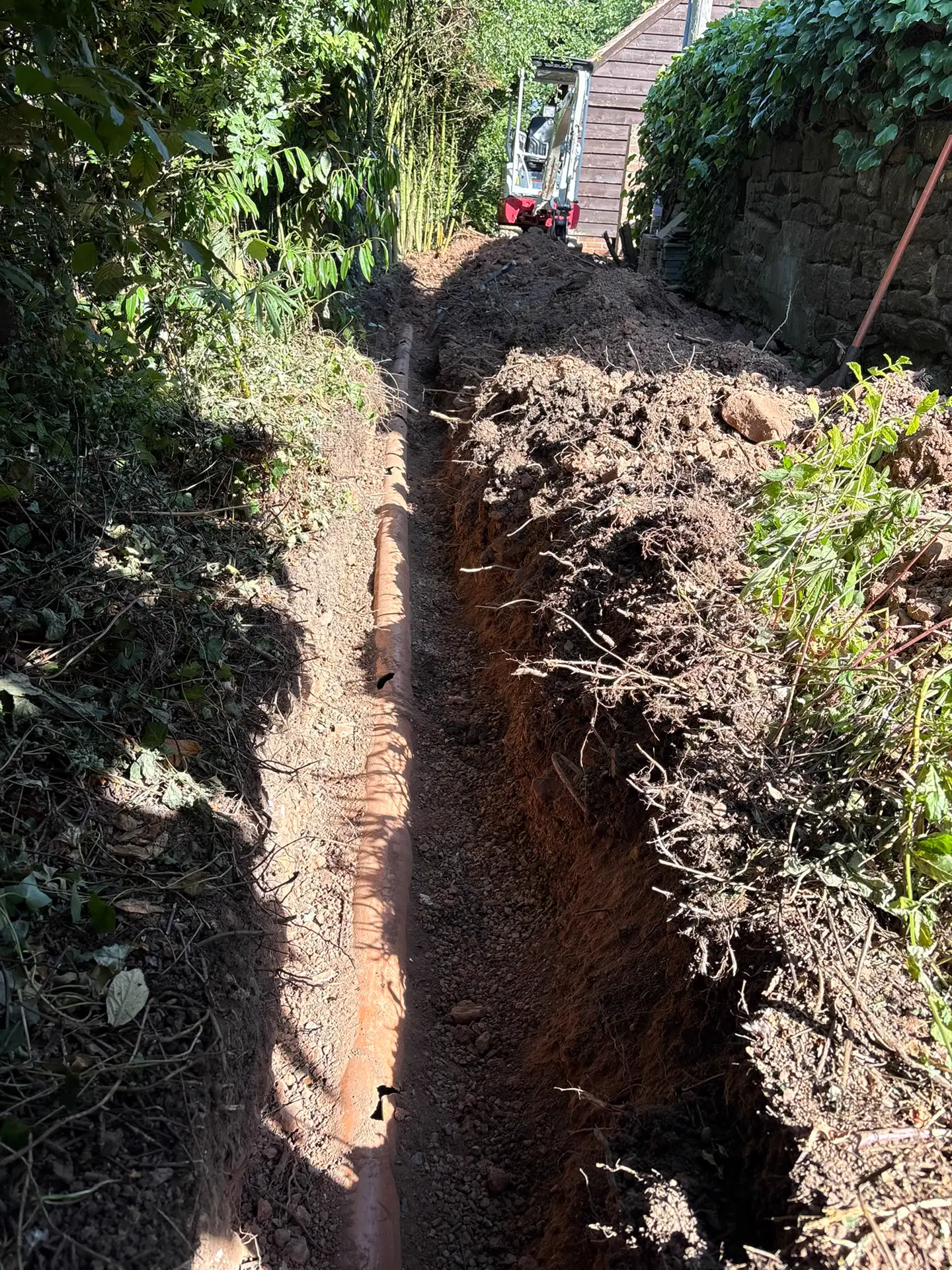 New drainage run being laid in a trench between a hedge and stone wall